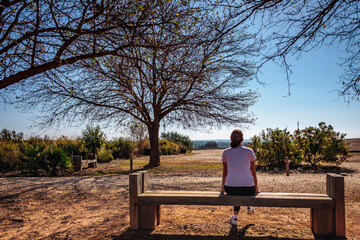 young girl sitting on her back on a bench by a tree