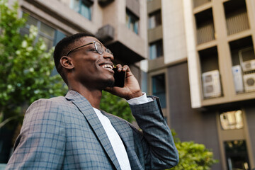 Joyful african american man talking on mobile phone while walking on street