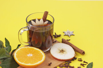 Delicious mulled wine and ingrediets on yellow background.Hot red beverage in glass mug with christmas spices, anise, orange and apple slice, cinnamon sticks.Holiday christmas hygge and homely concept