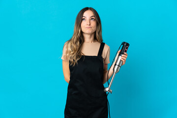 Romanian woman using hand blender isolated on blue background and looking up