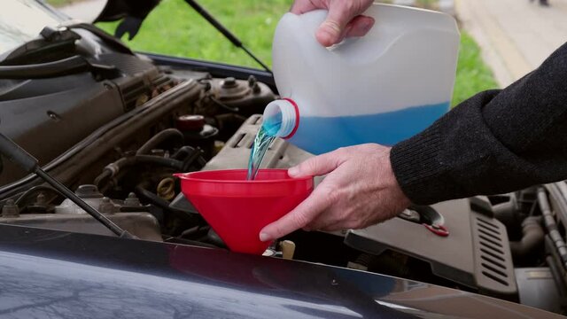 Driver pouring windshield washer fluid to car