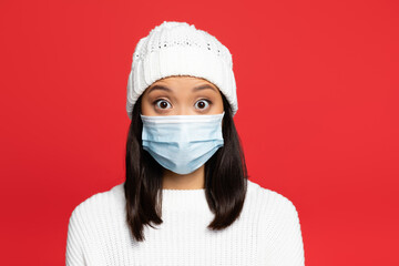 shocked asian woman in medical mask and hat isolated on red