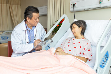 Confident Asian medical doctor explaning to cheerful female patient on medical condition lying on...