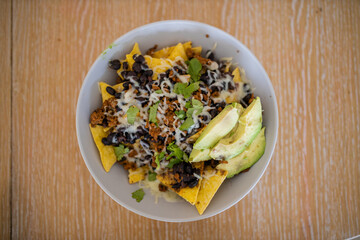 Bowl of nachos with avocado and beans on a wooden table
