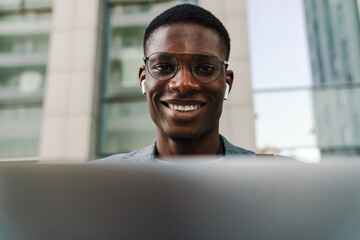 Cheerful african american man in earphones smiling and using laptop