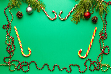 Christmas frame with, sugar colored candies and sprigs of pine with decorations on a green background place for an inscription.
