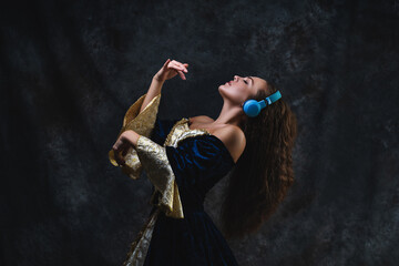 Beautiful woman in renaissance dress listens to music in wireless headphones on abstract dark background