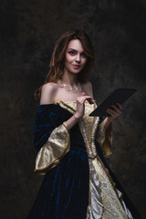 Beautiful woman in renaissance dress uses tablet on abstract dark background