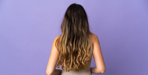 Fototapeta premium Young caucasian woman isolated on purple background in back position