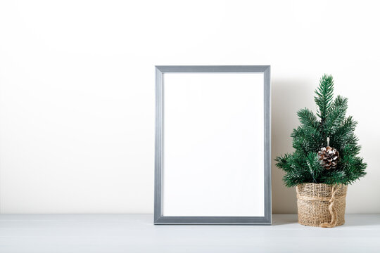 Photo or poster mockup with a silver frame, small decorative christmas tree on wooden table