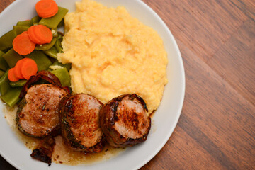 top down closeup of pig medailions with vegetables and polenta with wooden background