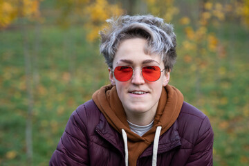 Young woman with stylish short hair, dressed in a gender neutral style.  New femininity. Style Element - Red Sunglasses