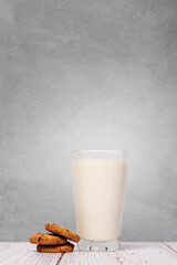 Chocolate chip cookies sitting next a full glass of milk on a wood surface against a textured wall background with copy space and room for text on a vertical image