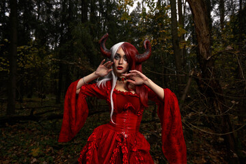Maleficent Woman in Red Clothing and Horns in dark Forest. Posing in magik forest