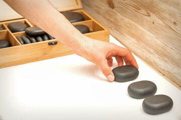 Hand of masseur lays out massage stones on the table in spa salon