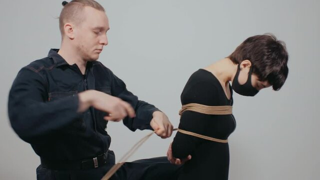 Shibari Training. Shibari master ties a young Caucasian woman with ropes.