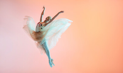 Ballerina in a light light dress flying in jump on an illuminated colored background