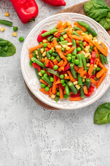 Various steamed vegetables top view. Boiled peas, corn, string beans, carrots, and peppers in a white plate on a gray concrete table. Copy space for text. Diet and vegan food.