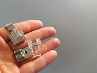 A set of feet for an electric sewing machine in a female hand. Gray backdrop. Standard sewing or...