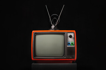Retro old red TV with antenna on black wooden box on black background