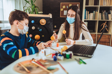 Happy school boy and girl with protective mask making a solar system for a school science project at home