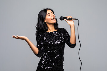 Beautiful brunette woman singing to microphone isolated on gray background