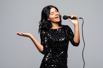 Portrait of happy young woman singing with microphone isolated on gray background