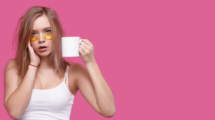 Woman with headache and hangover holding cup with hot drink on pink isolated background