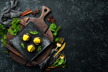 Yellow mango desserts "macaroons" on a black plate with mint. Top view. Rustic style.