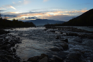 Beautiful landscape with high mountains with illuminated peaks, stones in mountain lake, reflection, blue sky and yellow sunlight in sunrise.