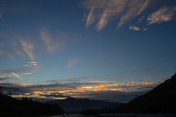Beautiful landscape with high mountains with illuminated peaks, stones in mountain lake, reflection, blue sky and yellow sunlight in sunrise.