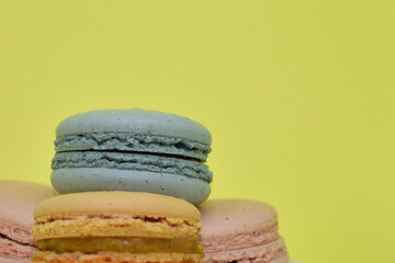 Multicolored macaroons in the form of a tower on a yellow background. Colorful greeting card with delicious almond cookies. Sponge cakes on top of each other. Spaces for text, copy space.