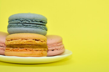 Multicolored macaroons in the form of a tower on a yellow background. Colorful greeting card with delicious almond cookies. Sponge cakes on top of each other. Spaces for text, copy space.