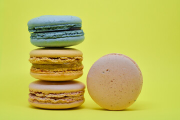 Multicolored macaroons in the form of a tower on a yellow background. Colorful greeting card with delicious almond cookies. Sponge cakes on top of each other. Spaces for text, copy space.