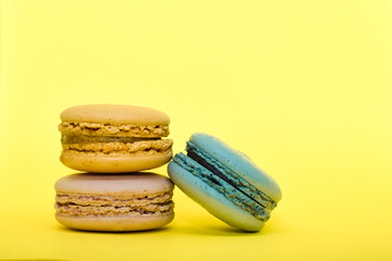 Multicolored macaroons in the form of a tower on a yellow background. Colorful greeting card with delicious almond cookies. Sponge cakes on top of each other. Spaces for text, copy space.