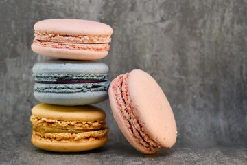Multicolored macaroons cakes in the form of a tower on a dark gray concrete background. Macaroons on a gray concrete background. Cakes on top of each other. Space for text, copy space.