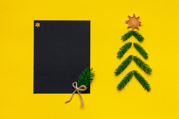 Black paper mockup of New Year wish list near handmade Christmas spruce on yellow background