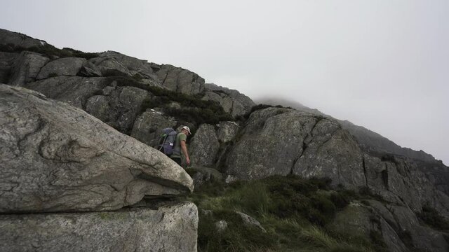 A person climbing a big boulder in the Welsh mountains on a foggy day