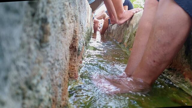 tourists dip feet in thermal canal water of Bagno Vignoni, Italy. Low-angle
