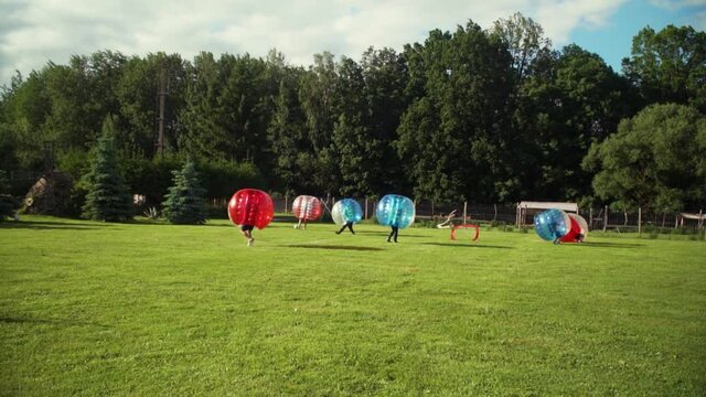 A young group of men is playing Bubble football in the park, one of them scores a goal after the pass from the corner kick.