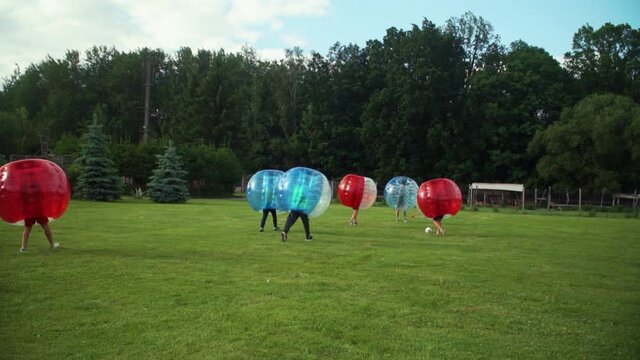 A young group of men is playing bubble football in the park, they are bumping into eachother.