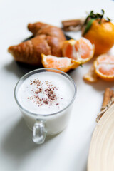Composition with New Year's assortments on a white table. Christmas mood. on a white background coffee croissant tangerines and Christmas red balls. Close-up in the foreground of a mug with milk.