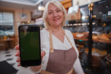Selective focus on a smart phone with copy space in the hand of female baker at her bakery store