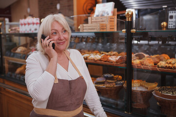 Cheerful female baker talking on the phone, working at her bakery shop, copy space