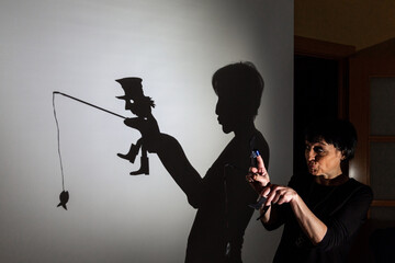 play shadow projected against a white background. a homeless man with a rod fishing