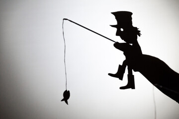 play shadow projected against a white background. a homeless man with a rod fishing