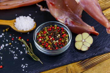 Whole raw rabbit meat with spices on a black slate cutting board on wooden table