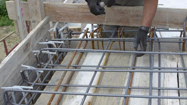 worker using steel wire and pincers to secure rebar before concrete is poured over it.
