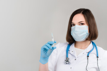 Portrait of young beautiful doctor shows syringe in hands on light background