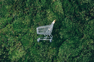 Shopping cart on green grass, moss background. Top view. Minimalism style. Creative design. Shop trolley. Sale, discount, shopaholism, ecology concept. Sustainable lifestyle, conscious consumption - obrazy, fototapety, plakaty
